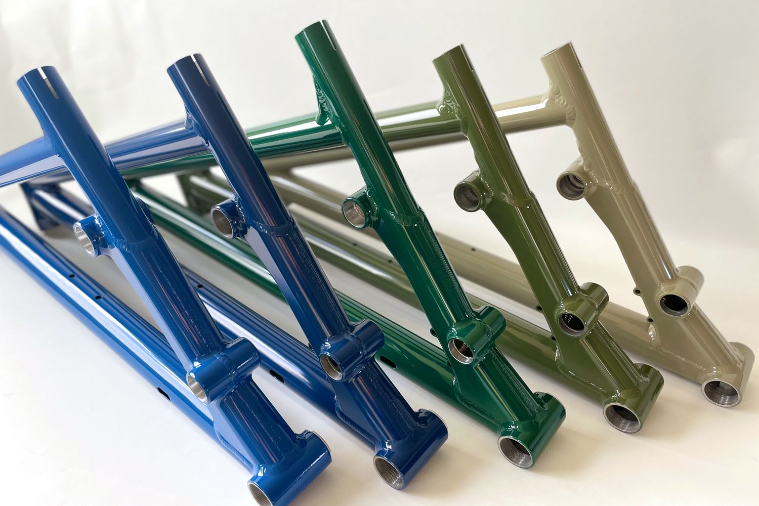 Eine Sammlung bunter Fahrradrahmen in Blau, Grün, Hellbraun und Oliv, die nebeneinander