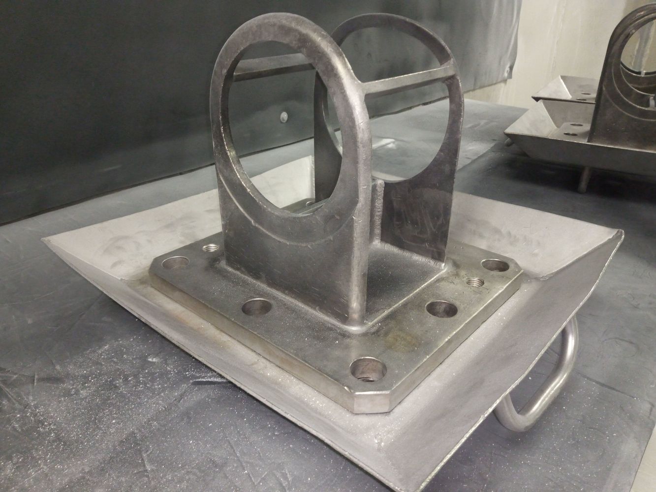 Ein metallisches Bauteil mit einem kreisförmigen Ausschnitt, das auf einer flachen Basis mit mehreren Löchern montiert ist